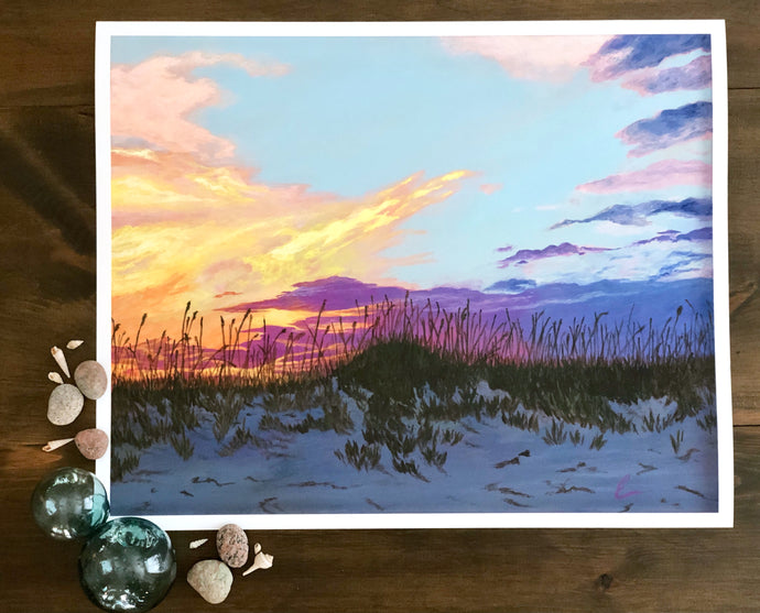 print of painting of peach, gold, and purple sunset in front of pale blue sky over darkening sand dunes with sea oats surrounded by shells, stones, and glass baubles